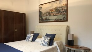 A bedroom with a large bed, a wooden wardrobe, a nightstand, and a painting on the wall.