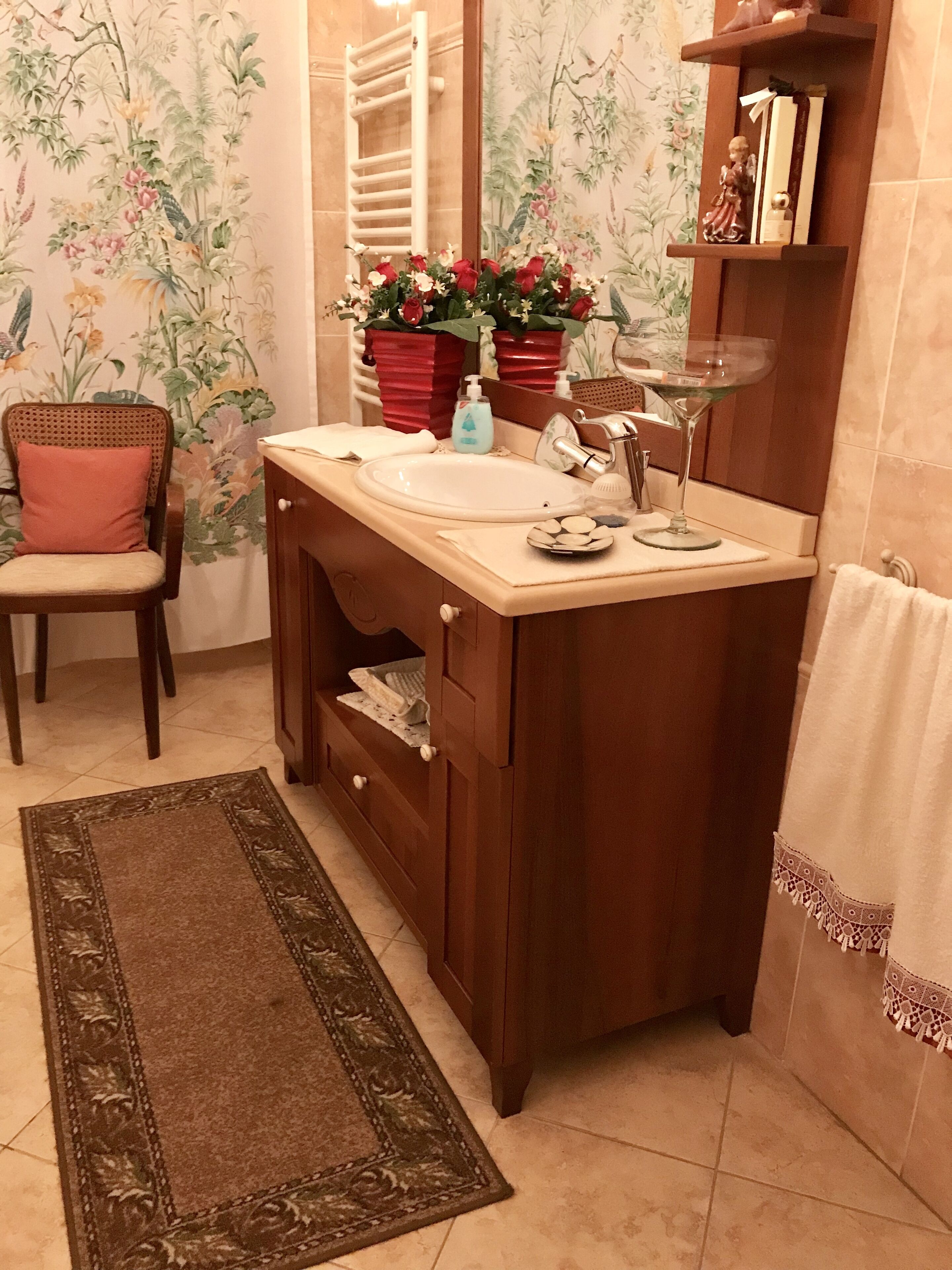 A bathroom with a wooden vanity, a sink, a mirror, a towel rack, a chair, and a decorative rug.