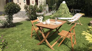 A patio with a wooden table and chairs, a white teapot, and a striped lounge chair.