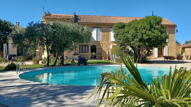 A pool area with a stone building, outdoor furniture, and trees.