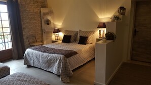 A bedroom with a large bed, two bedside lamps, a nightstand, a window with curtains, and a stone wall.