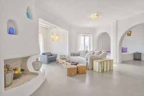 Relax in a comfortable seating area with a sofa and armchair, surrounded by a fireplace and natural light.