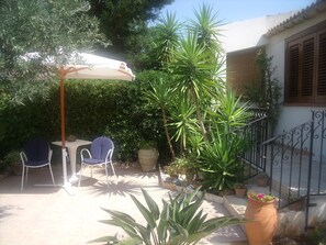 Un espace patio comprenant deux chaises, une table, un grand parasol et diverses plantes en pot.