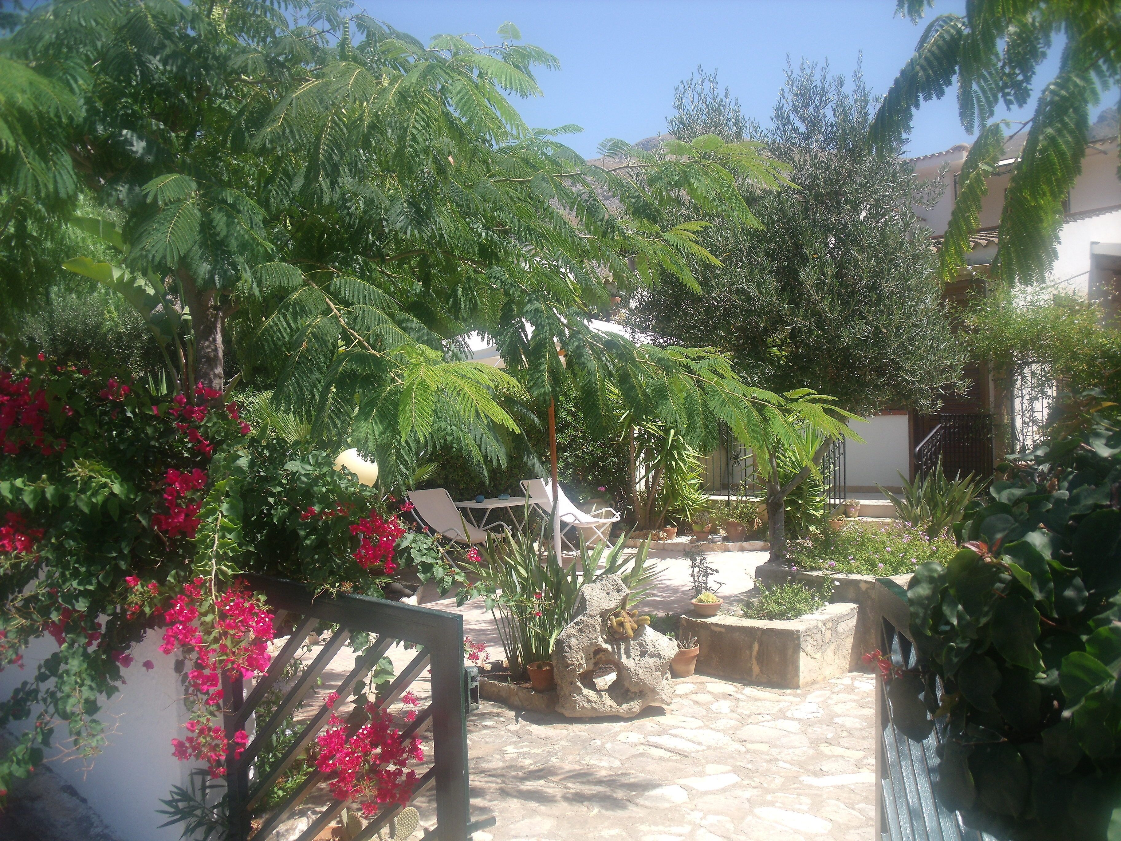 A courtyard with potted plants, a stone floor, and a metal gate.