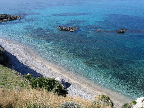 Un paysage côtier caractérisé par une eau d’un bleu limpide, des affleurements rocheux et une plage de galets.
