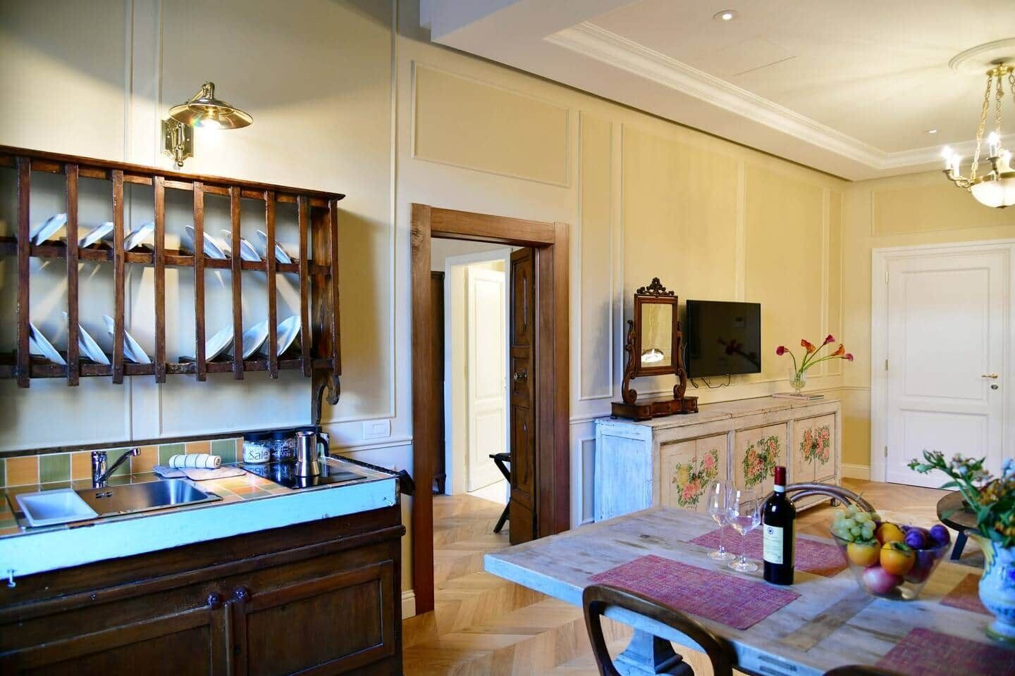 A dining area with a wooden table, chairs, a wine bottle, and a fruit bowl.