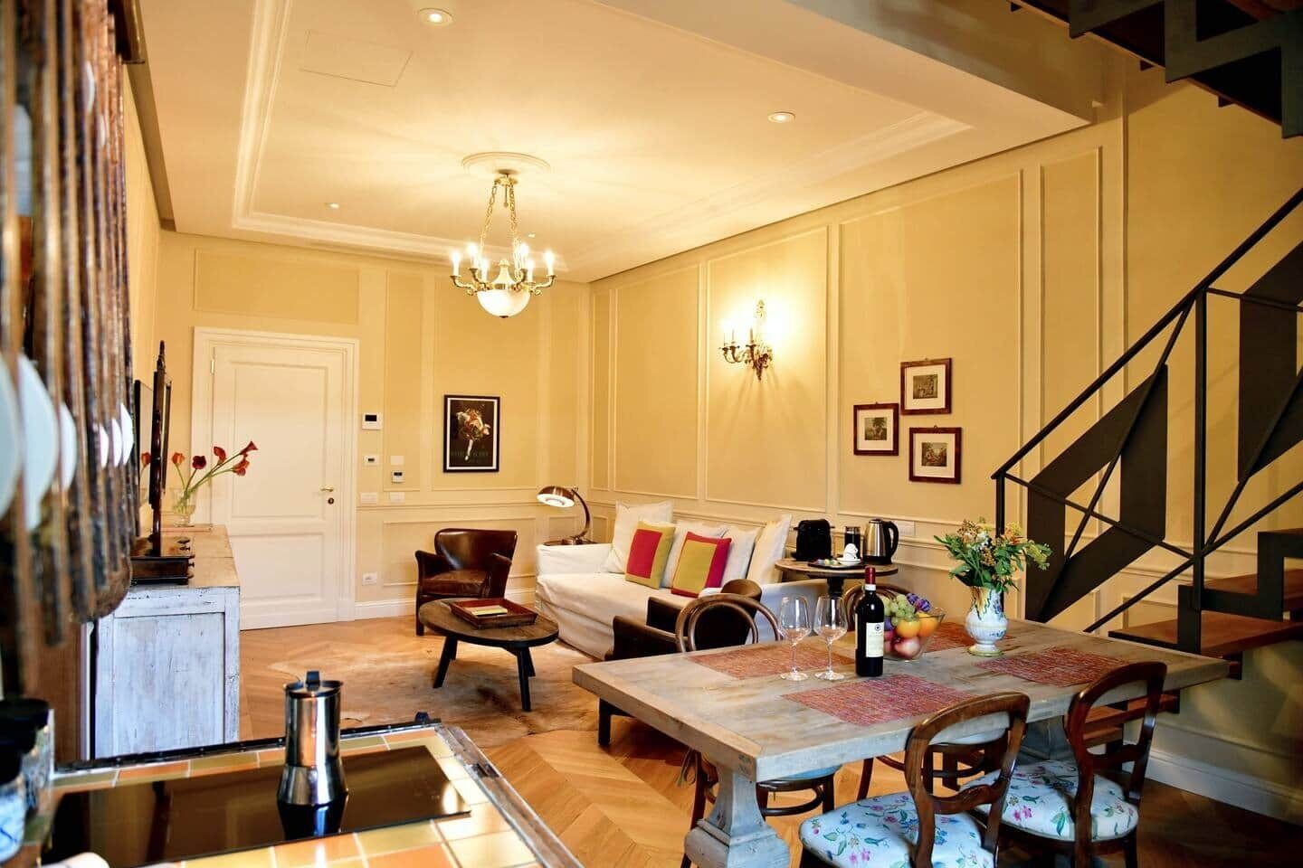 Ein Zimmer mit Esstisch, Stühlen, einer Couch, einer Chandelüster, einer Treppe und gerahmten Bildern an der Wand.