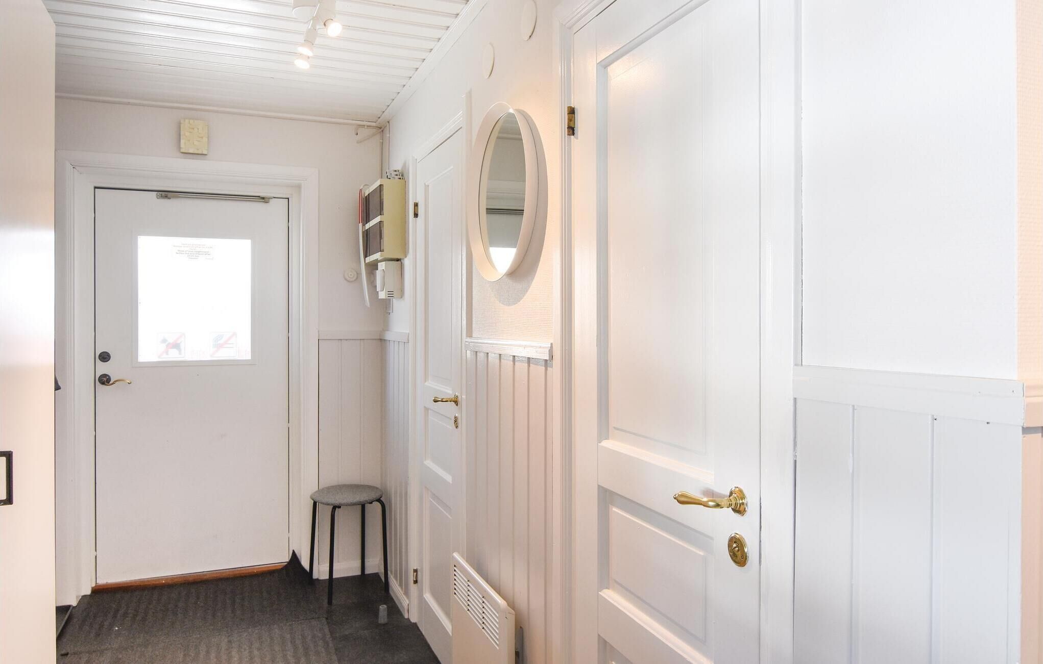 A hallway with white doors, a radiator, a small stool, and a mirror on one door.