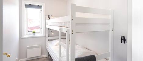 Dormitorio con literas, ventana, radiador y puerta.