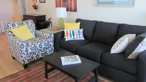 Un salon avec un fauteuil à motifs, un canapé foncé, une table basse sur laquelle se trouve un livre et une lampe.