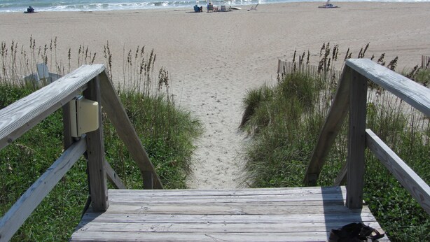 Une promenade en bois mène à une plage de sable, d’où l’on a une vue dégagée sur l’océan.