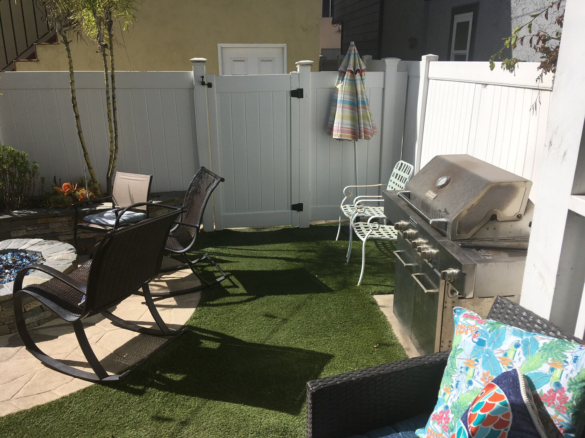 Un jardin avec un barbecue, deux chaises, une table et une clôture blanche.