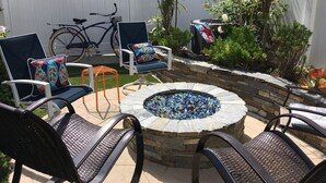 Un espace extérieur aménagé en patio, avec un foyer en pierre entouré de chaises et d’un vélo.