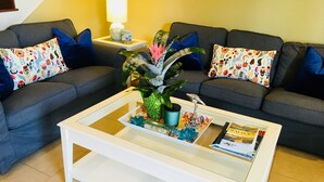 Un salon avec un canapé gris, des coussins bleus, une table basse blanche et une petite table d’appoint avec une lampe.