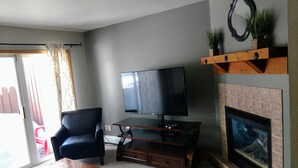 Een woonkamer met een flatscreen-tv, een open haard, een leren fauteuil en een salontafel.