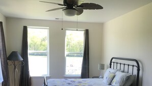 A bedroom with a bed, a ceiling fan, a window, and a floor lamp.
