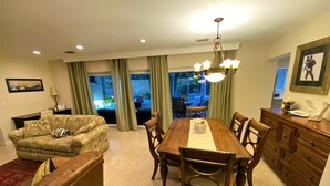 A dining area with a wooden table and chairs, a sofa, a TV, and a view of the outdoors through large windows. - Deerfield Beach House and Pool
https://my.matterport.com/show/?m=6txjncxb5Lo (Deerfield Beach)