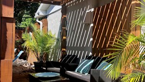Un espace extérieur aménagé en terrasse, doté d’une pergola en bois, de sièges confortables et de plantes en pot.