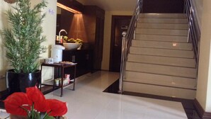 A hallway with a staircase, a potted plant, a small table with a bowl of red flowers, and a kitchen area with a sink and cabinets. - East Square Inn (Bacolod)