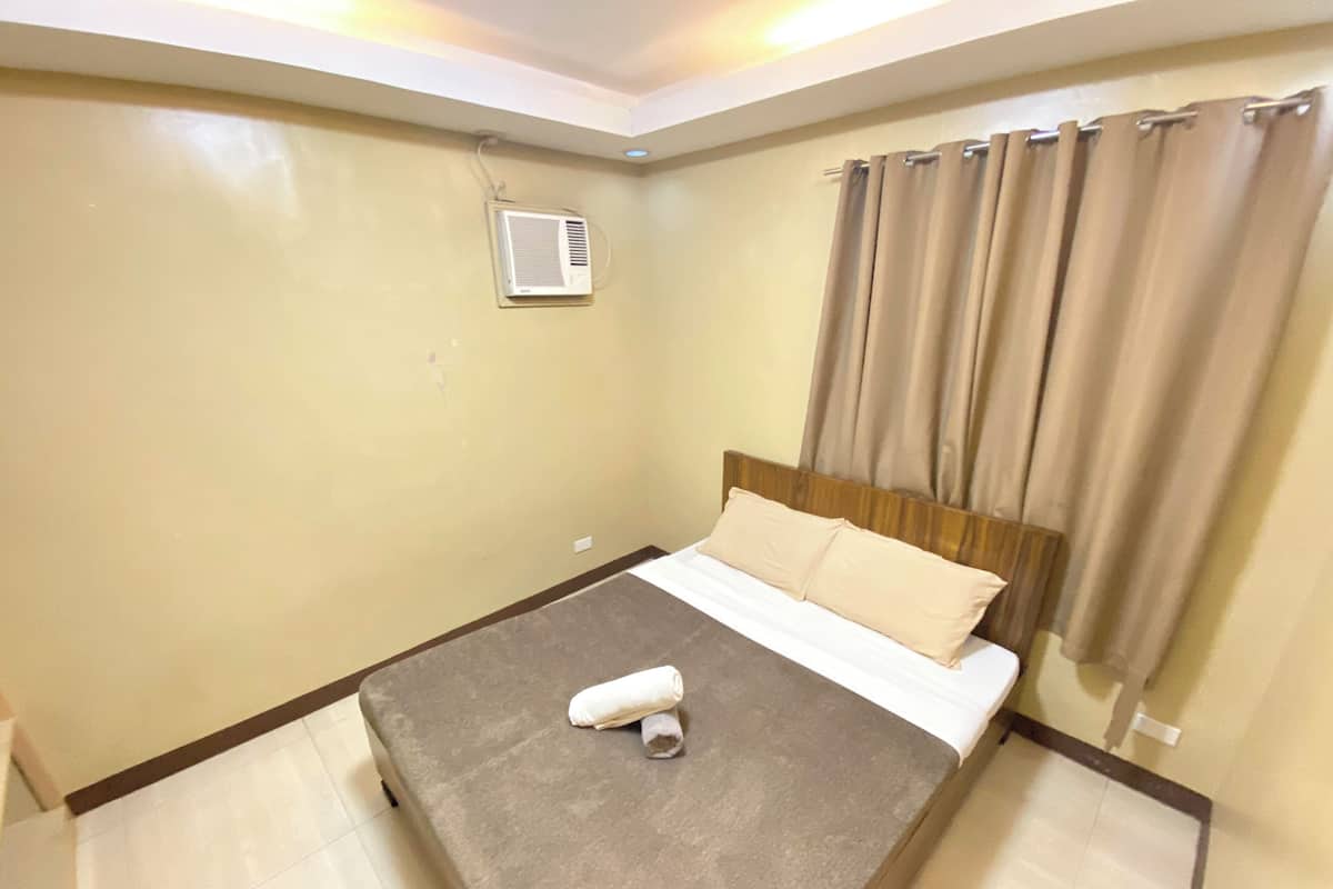 Um quarto com uma cama, ar condicionado na parede e uma janela com cortinas.
