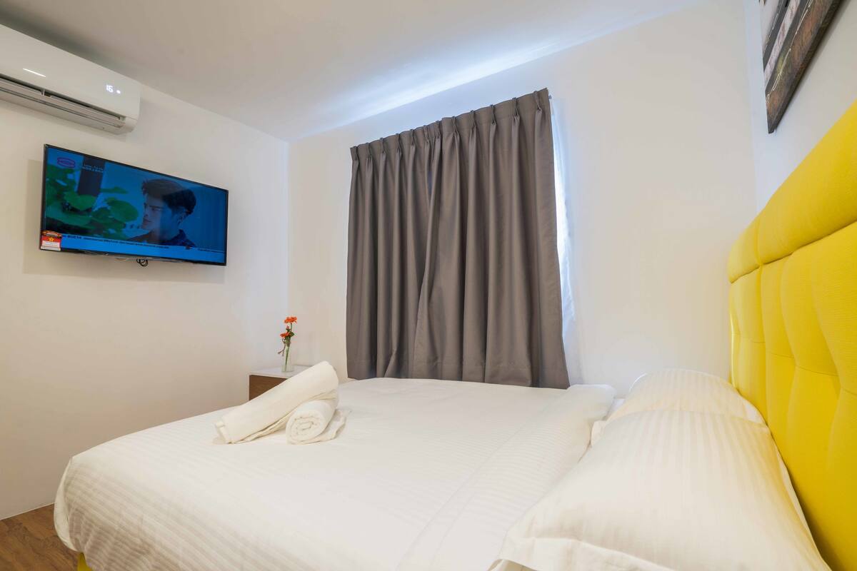 A hotel room with a bed, a television mounted on the wall, and a window with curtains.