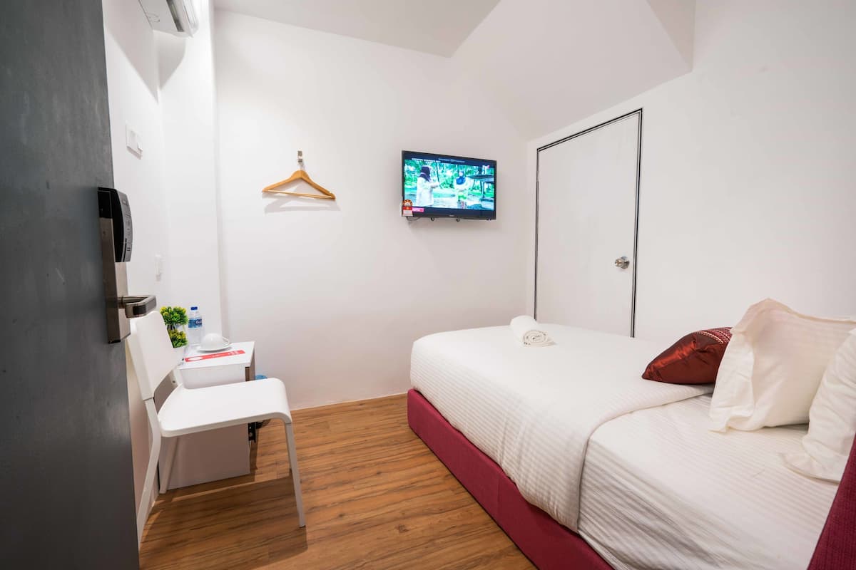A bedroom with a bed, a desk, a chair, a TV mounted on the wall, and a door.