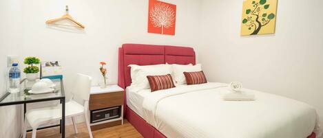 Habitación de hotel con cama, escritorio con silla, una mesita con planta y un perchero en la pared.