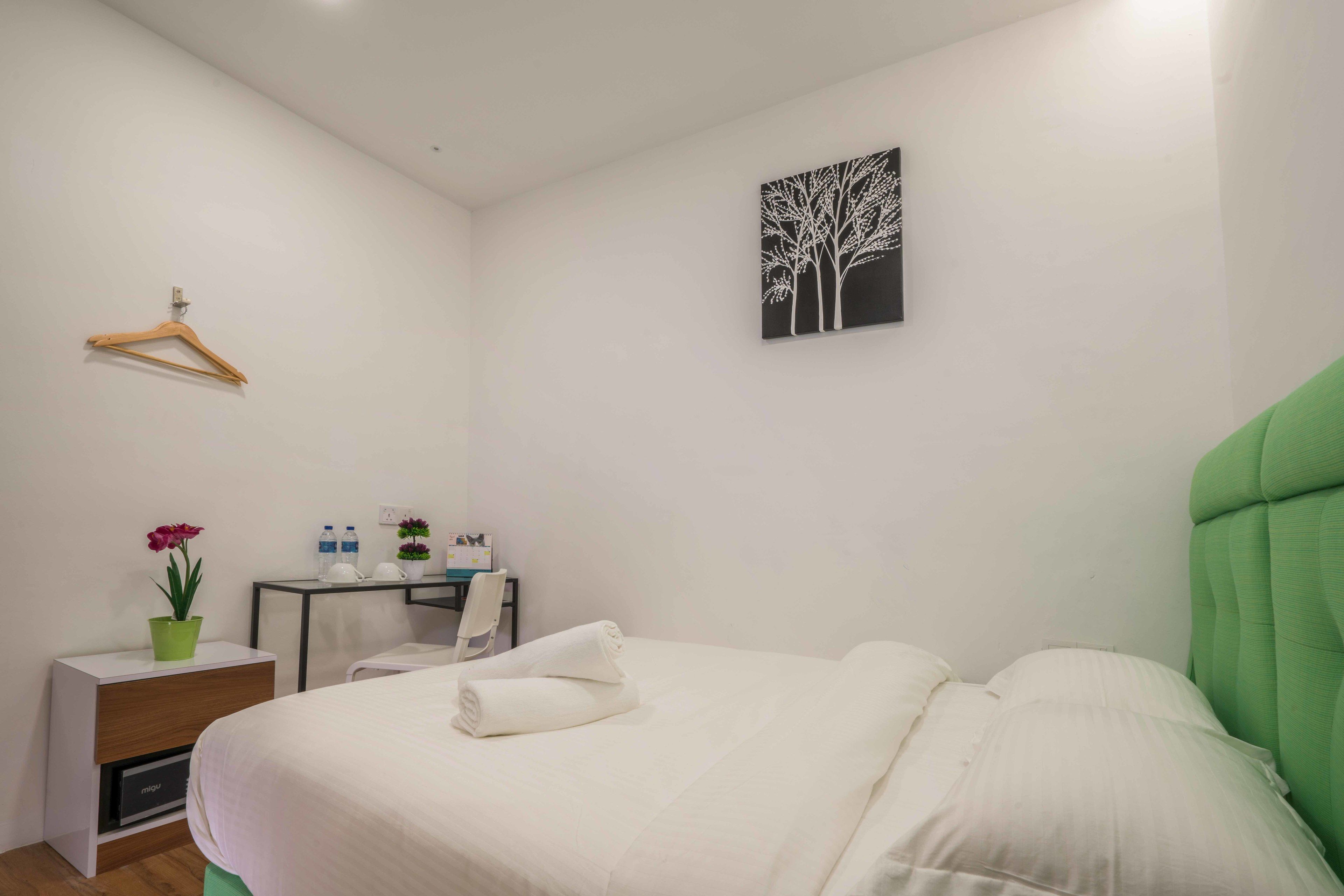 A neatly arranged bedroom with a bed, a desk, a chair, and a small table with toiletries.