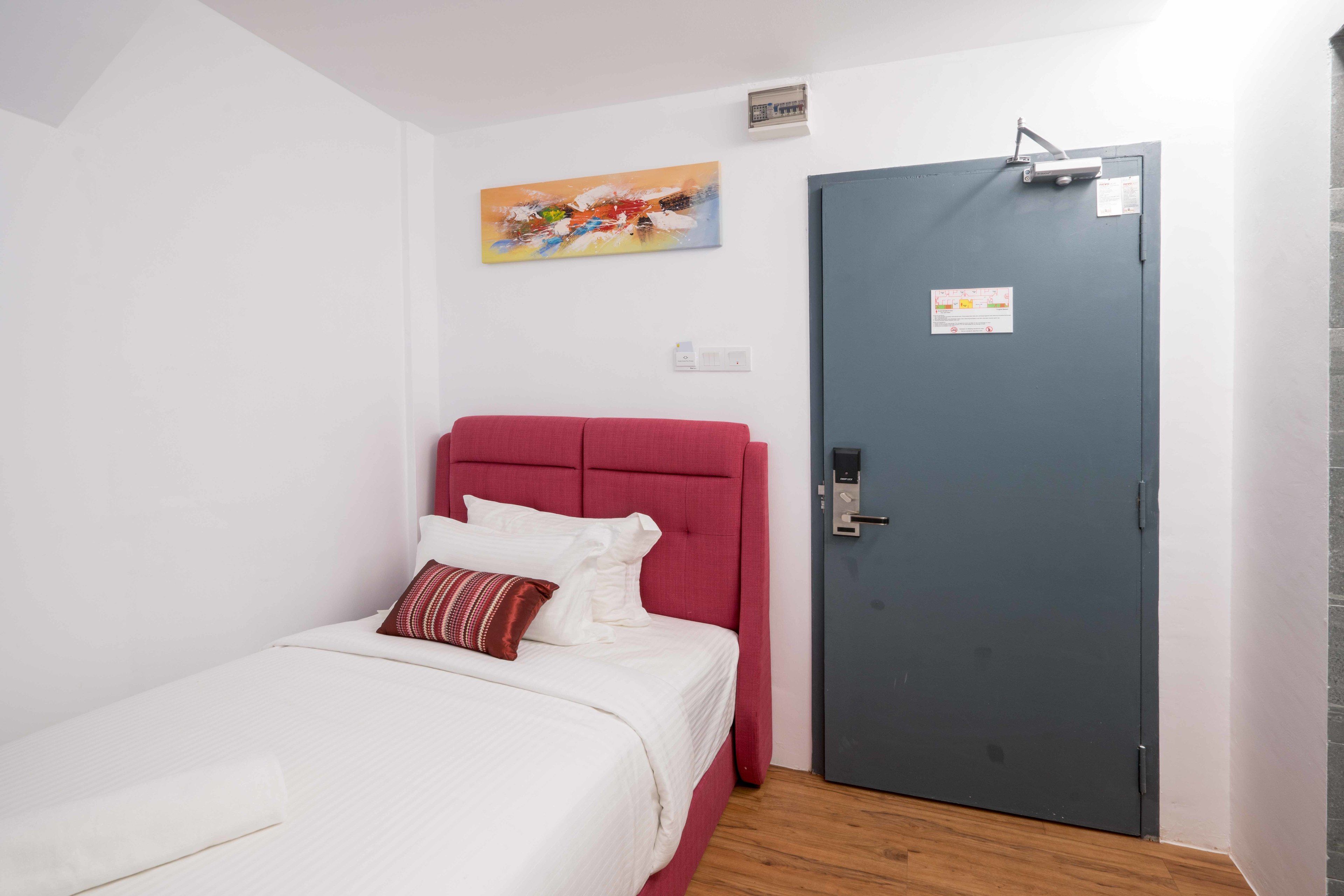 A room with a bed, a red headboard, a grey door, and a colorful abstract painting on the wall.