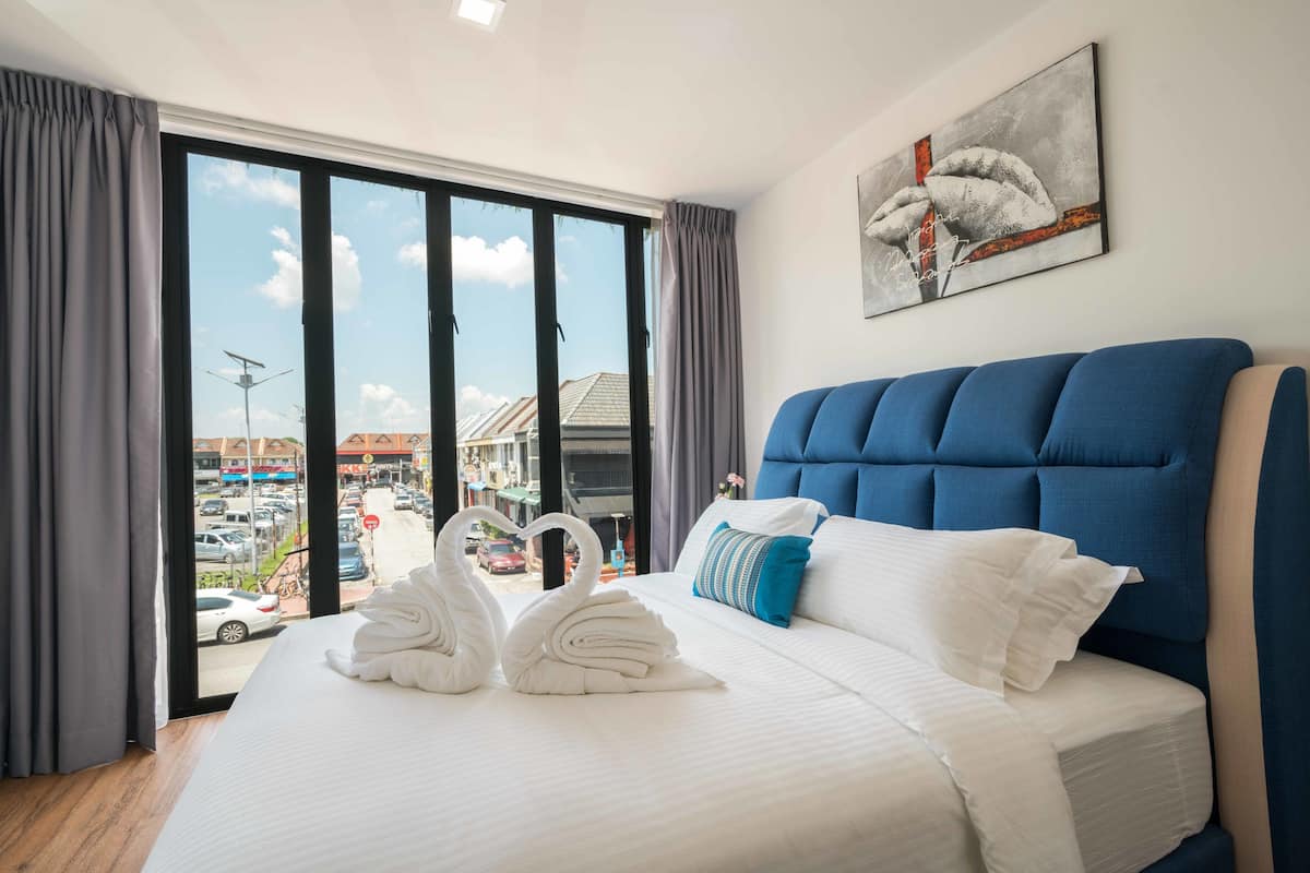 A hotel room with a large bed, a blue headboard, and a view of the street through a sliding glass door.