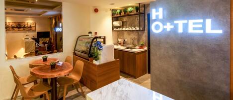 A hotel reception area with a marble table, wooden chairs, a reception desk, and a sign reading "HOTEL+TEL".