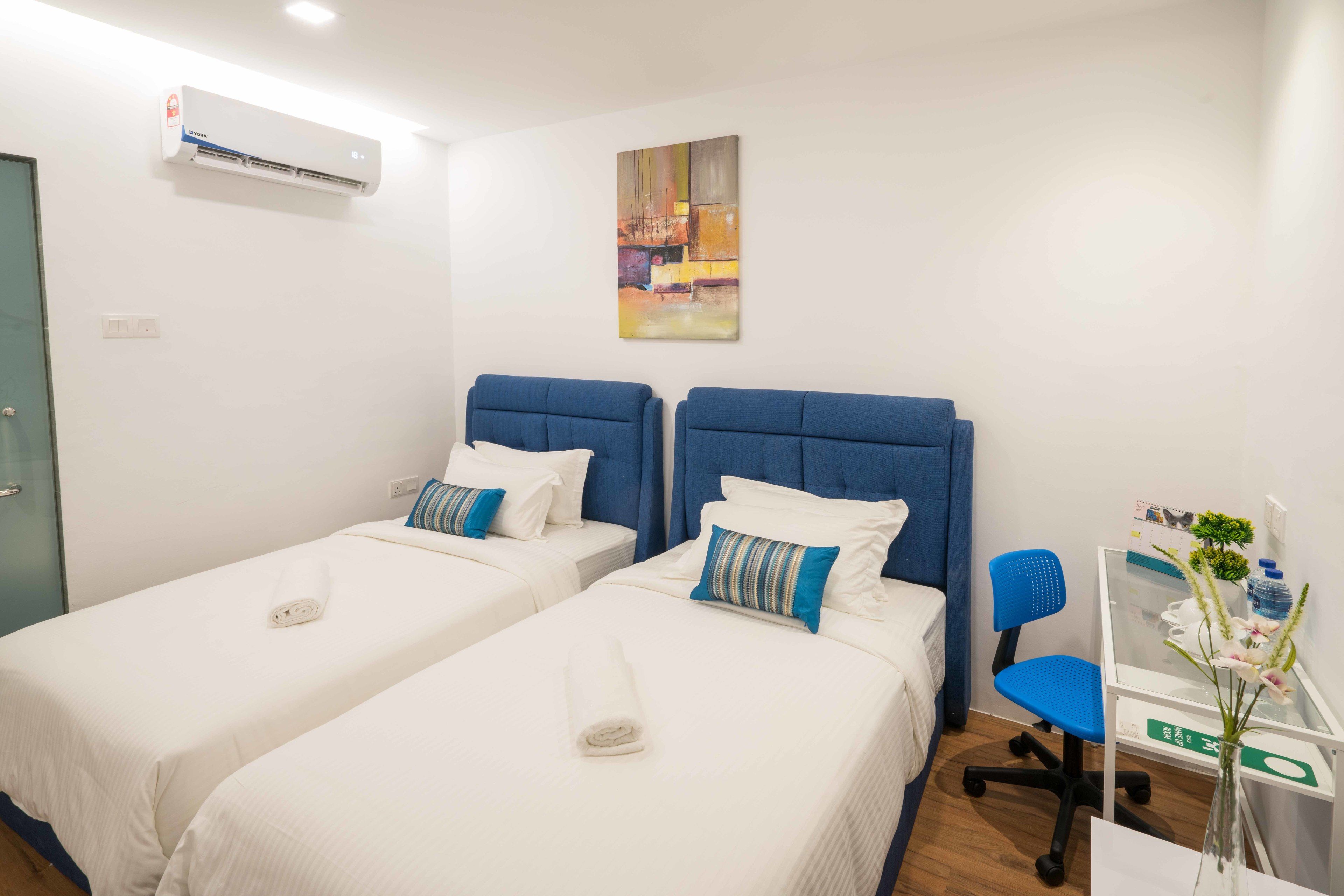 Una habitación de hotel con dos camas, un escritorio, una silla y aire acondicionado.