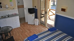 Habitación de hotel compacta con kitchenette, cama con ropa de cama a rayas, una pequeña mesa con sillas y vistas a través de un ventanal.