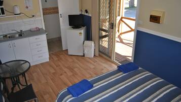 A compact hotel room with a kitchenette, a bed with striped bedding, a small table with chairs, and a view through a glass door.