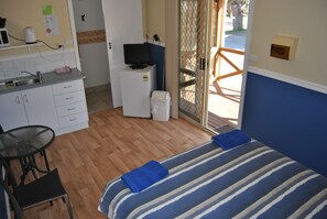 A compact hotel room with a kitchenette, a bed with striped bedding, a small table with chairs, and a view through a glass door. - Port Gregory Caravan Park (Gregory)