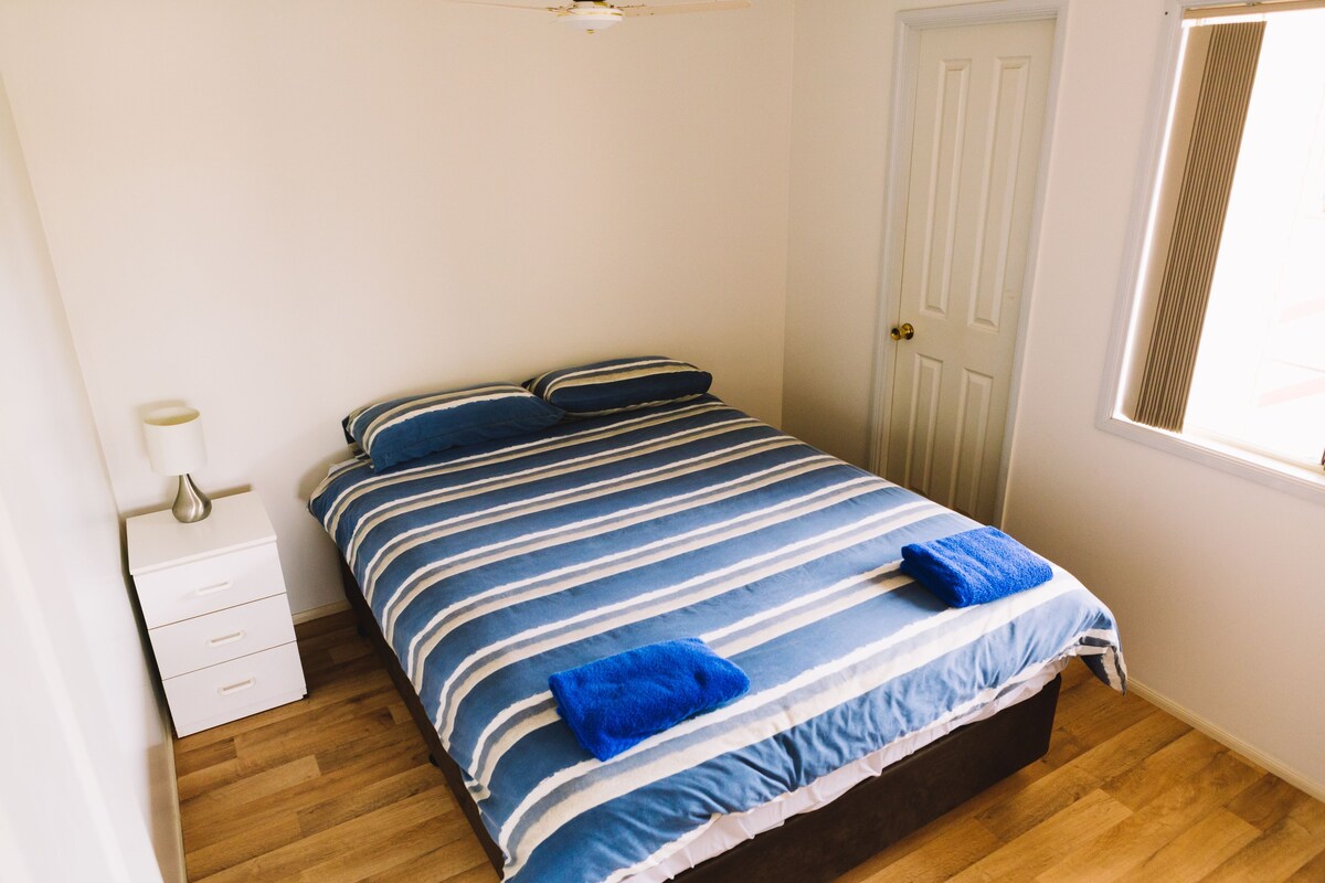 A bedroom with a bed, a nightstand, a window, and a door.