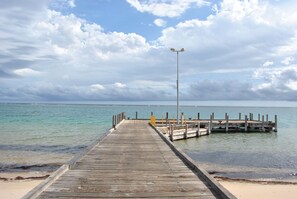 Un muelle de madera se adentra en aguas turquesas tranquilas, llegando a un embarcadero con un farol y un banco.