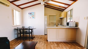 Una cocina compacta con piso de madera, un comedor con mesa y sillas, y un ventilador de techo.