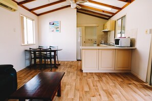 A compact kitchen with wooden flooring, a dining area with a table and chairs, and a ceiling fan. - Port Gregory Caravan Park (Gregory)