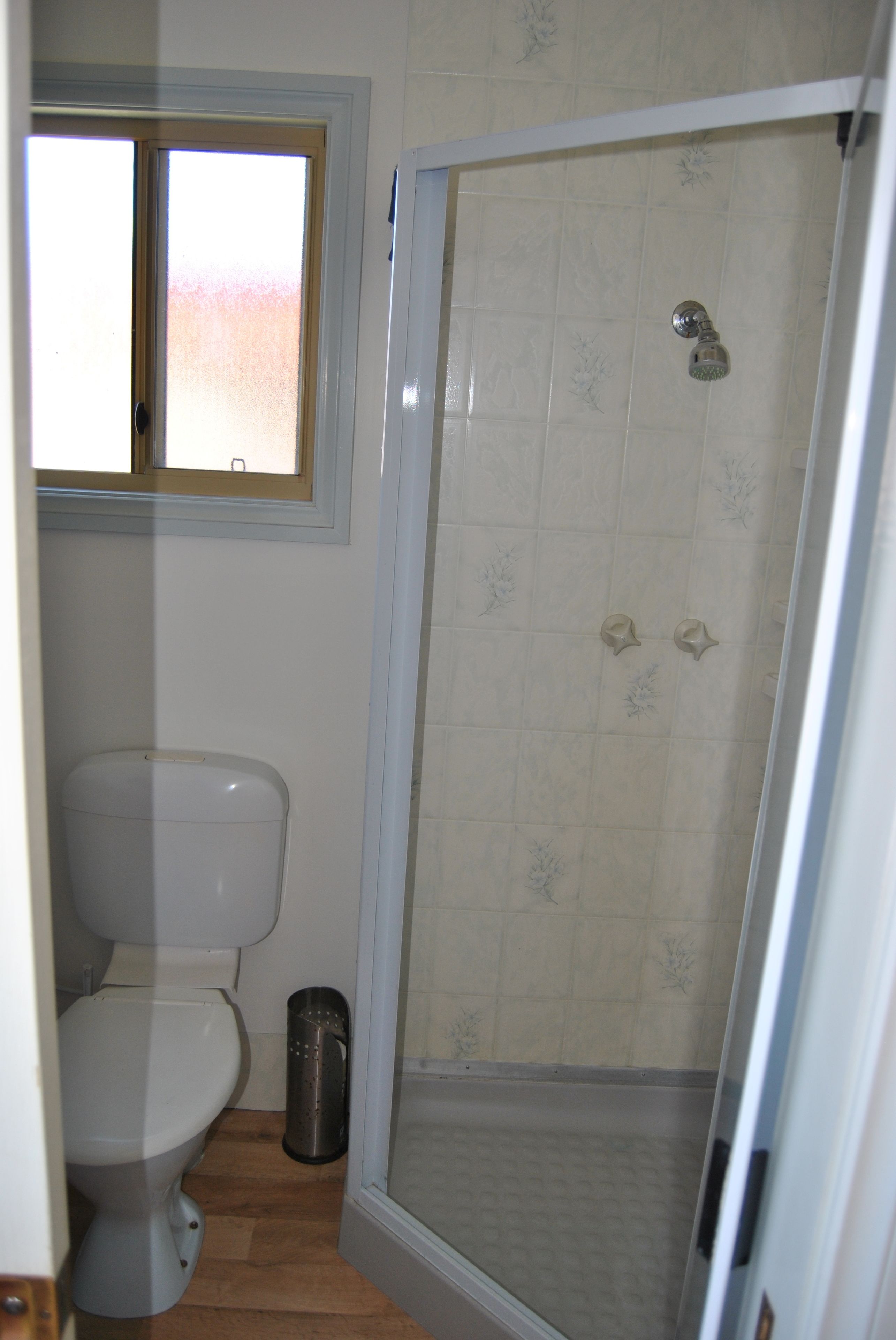 Ein Badezimmer mit Toilette, einer Duschkabine mit Glastür und einem Fenster über der Toilette.