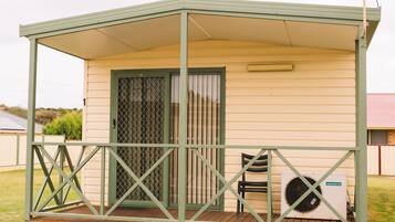 A small, single-story mobile home with a covered porch, a sliding glass door, and a patio area with a chair and an air conditioning unit.