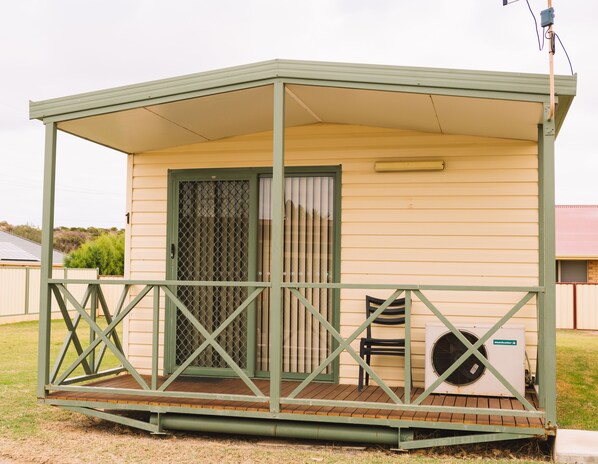 A small, single-story mobile home with a covered porch, a sliding glass door, and a patio area with a chair and an air conditioning unit.