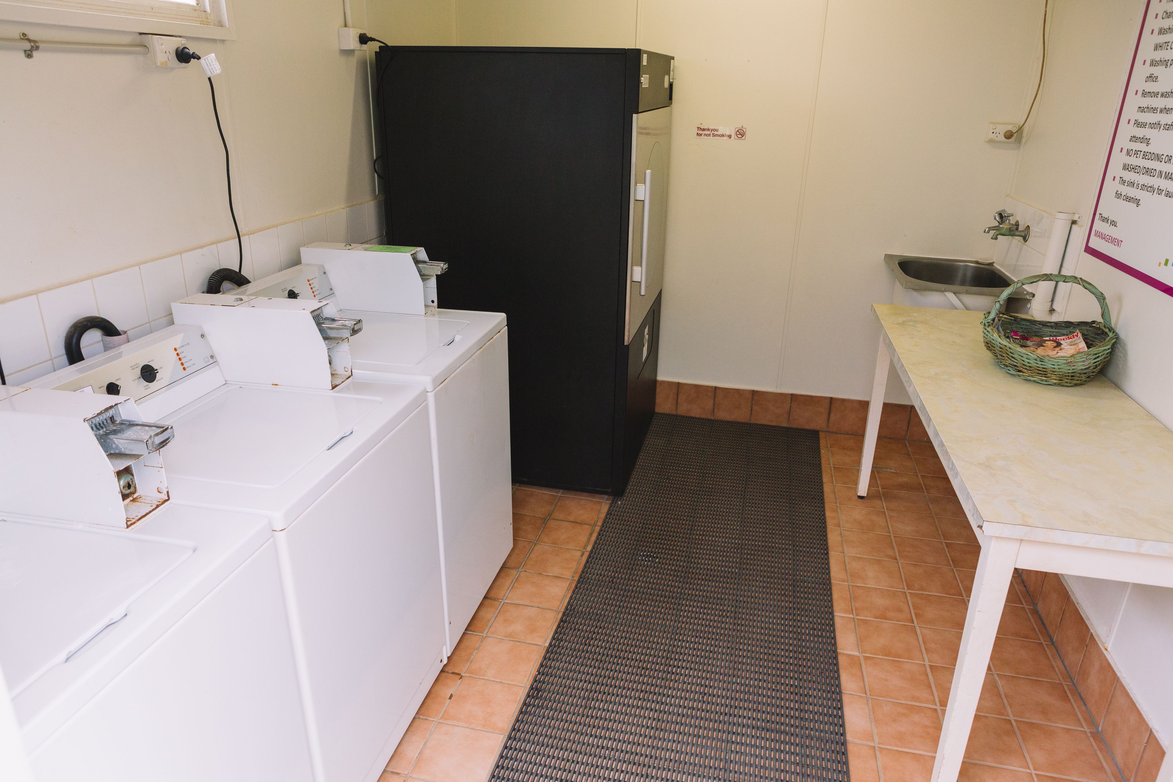 A laundry area with washing machines, a black refrigerator, a sink, and a small table with a basket.