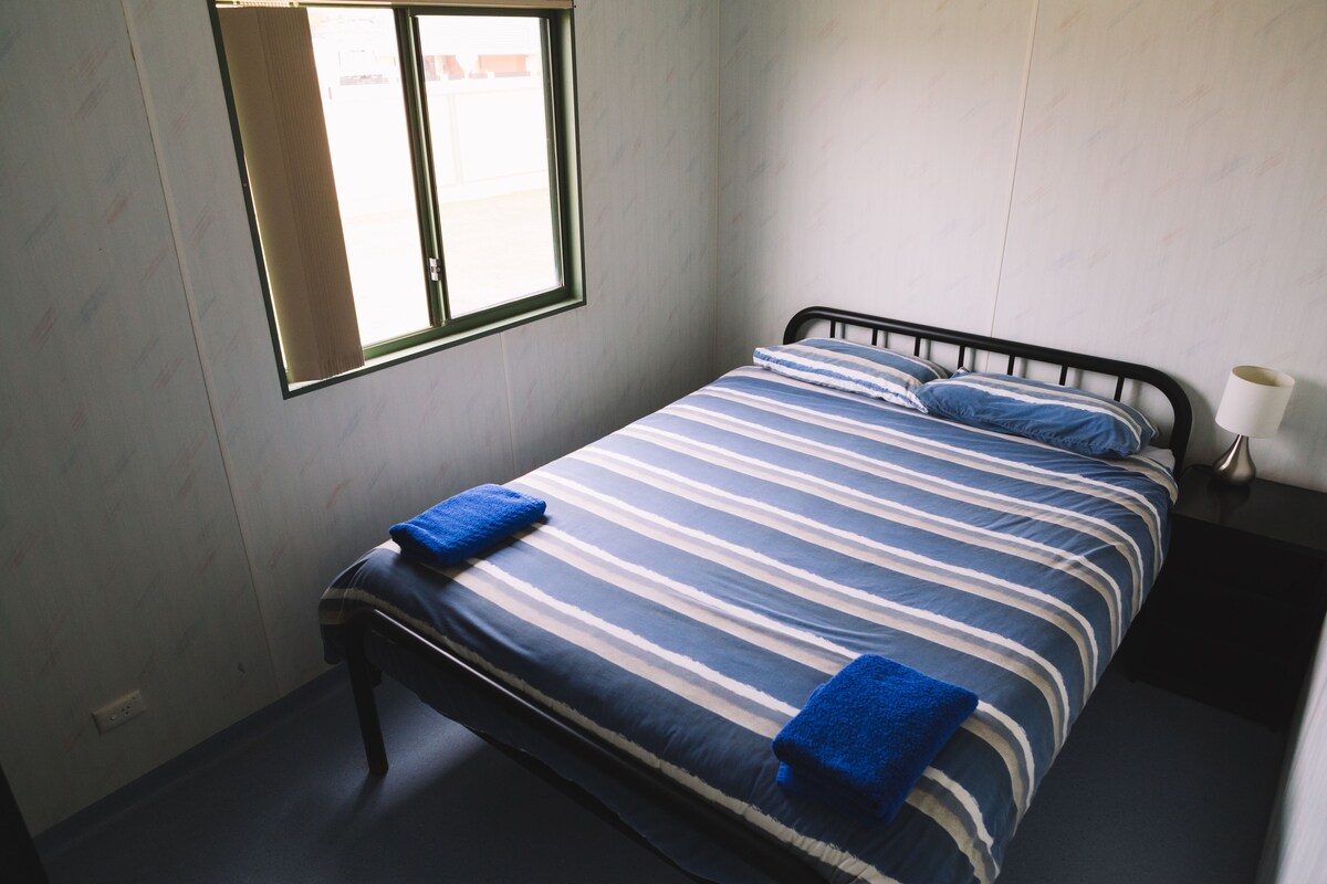 A bedroom with a bed, pillows, a window, and a bedside lamp.