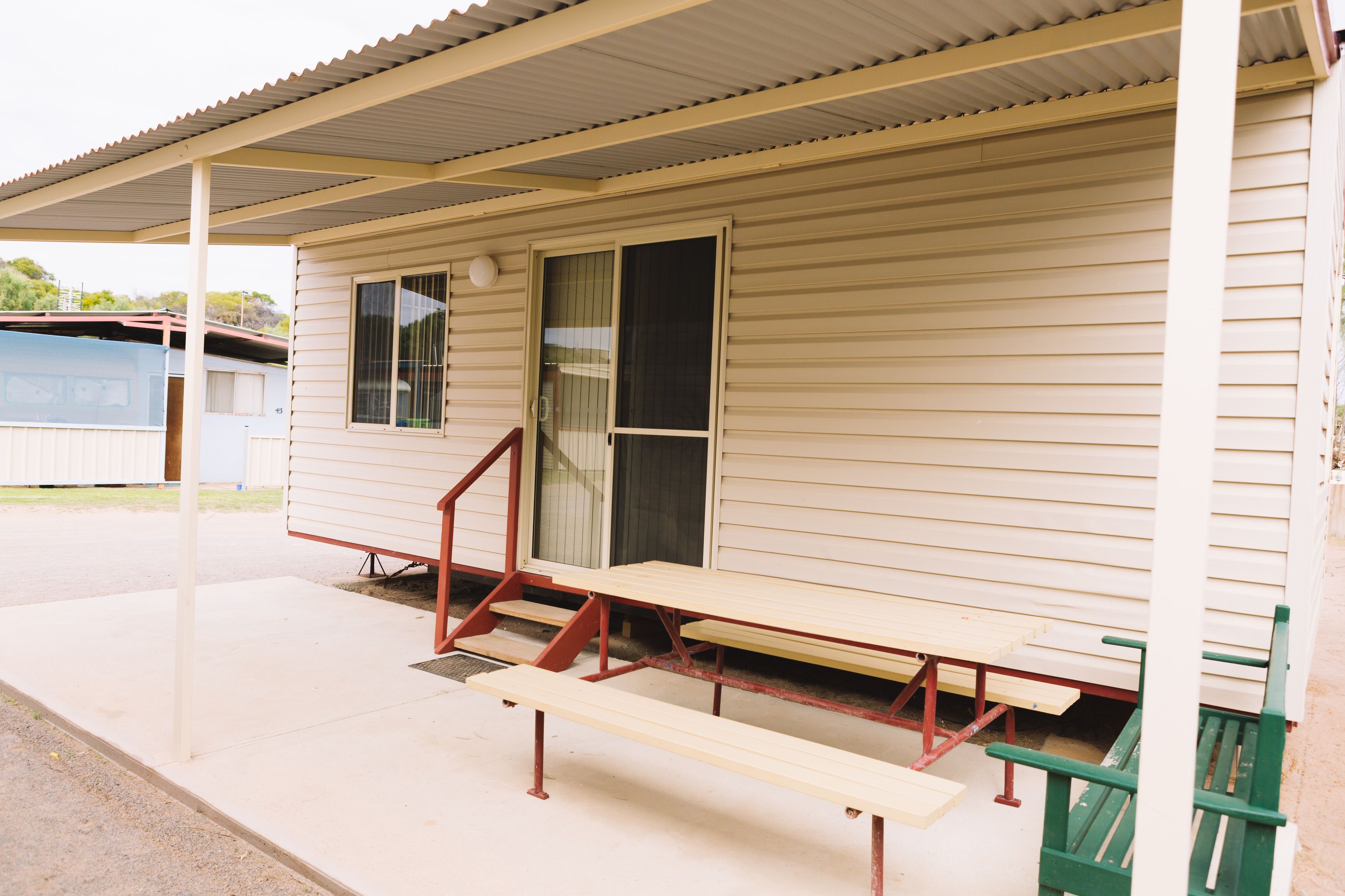 A single-story building with a covered porch, a set of stairs leading to a door, and a picnic table.