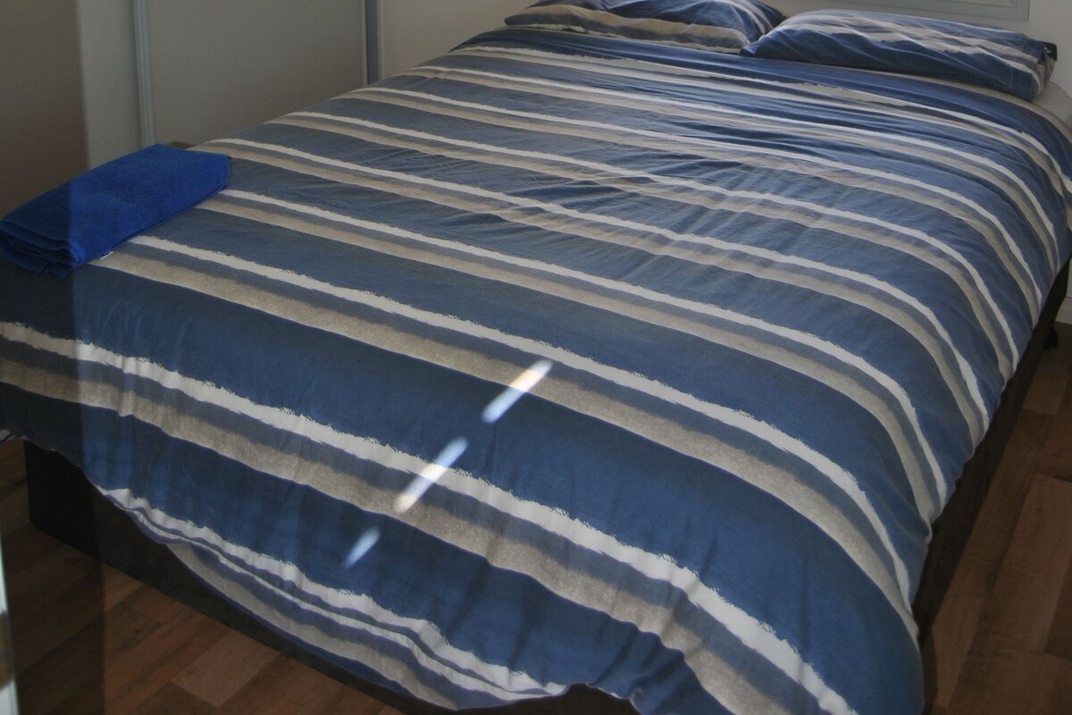 A bedroom with a bed, a window with blinds, an air conditioning unit, and a wardrobe.