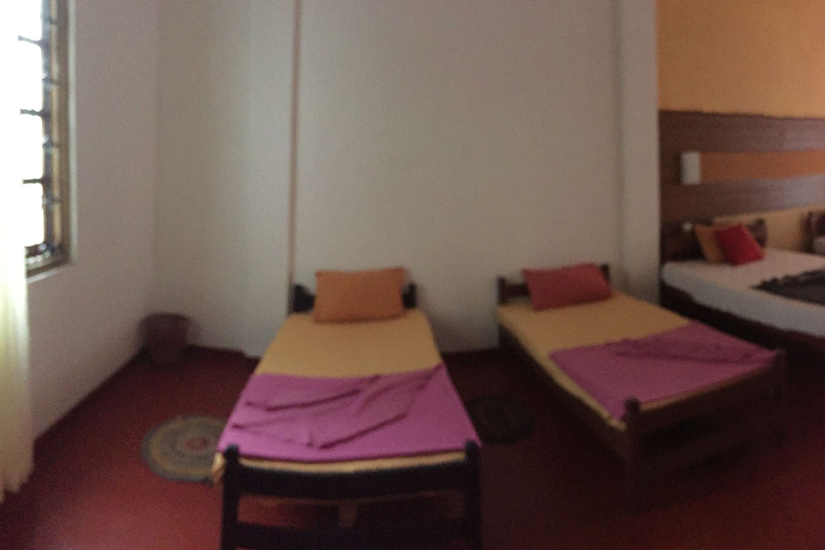 A room with three single beds, each with a pillow and a blanket. There is a wooden headboard on the right side of the room.