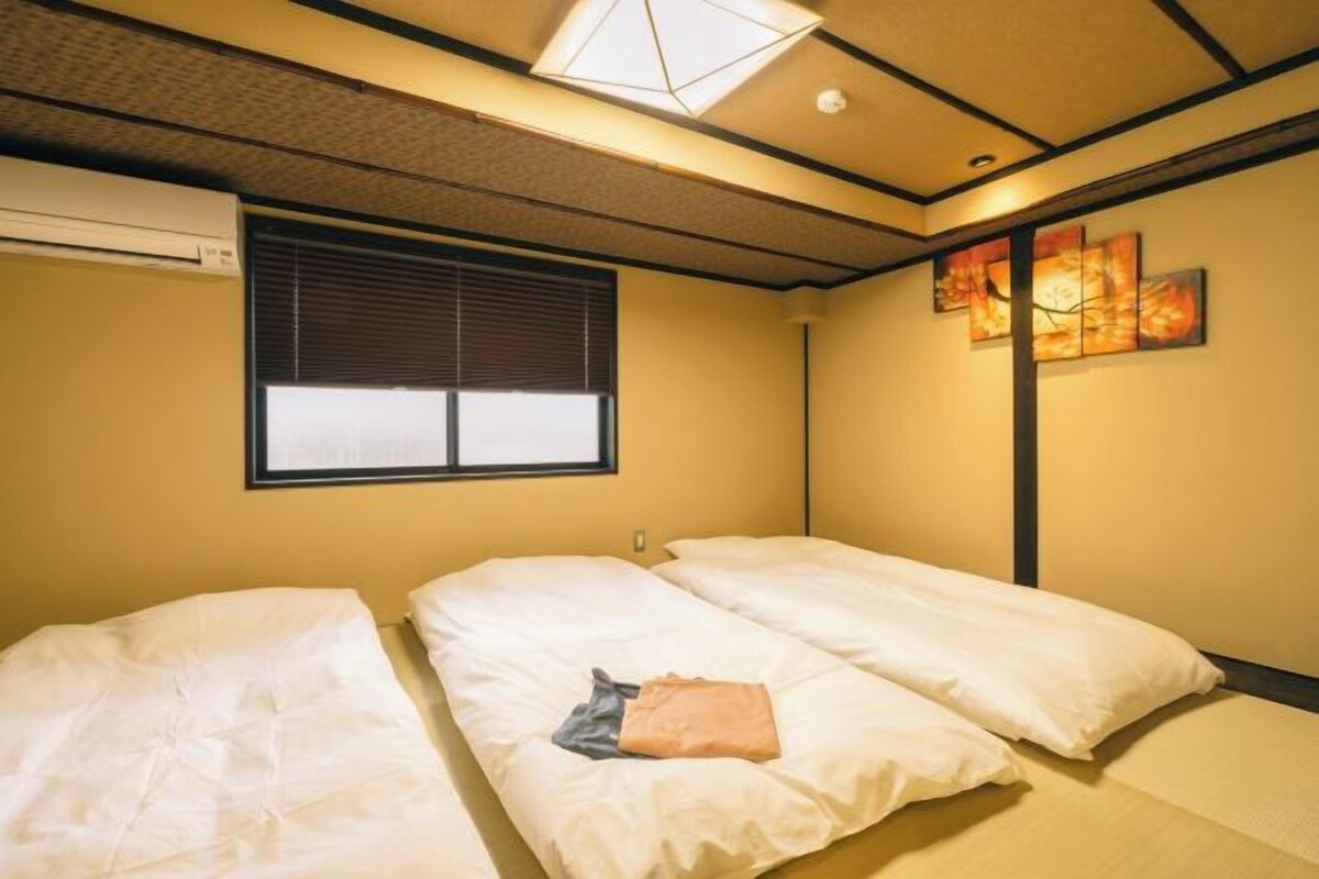 A hotel room with two beds, a window with blinds, a ceiling light, and a wall painting.