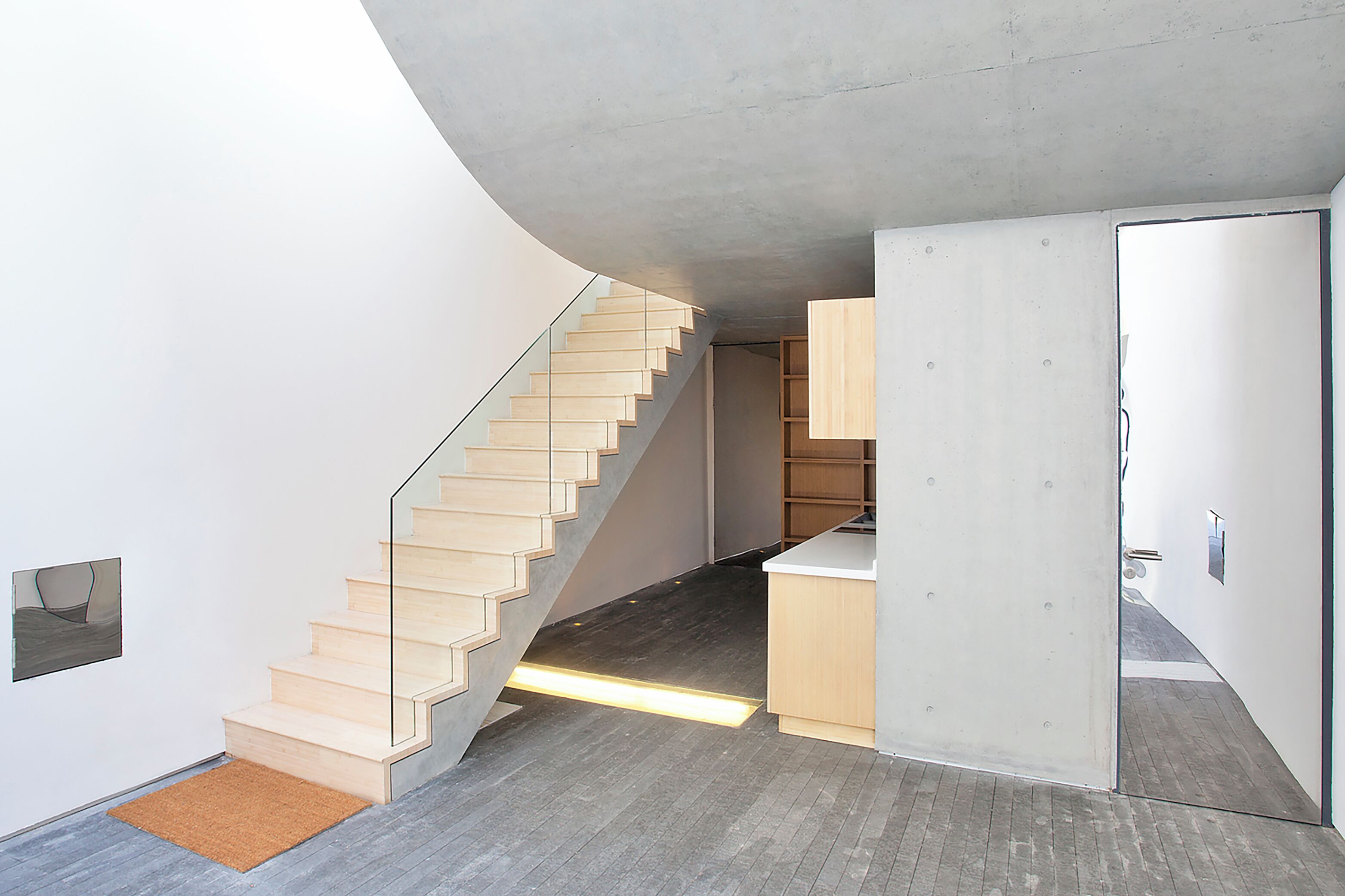Un interior moderno con una escalera de madera, una zona de cocina y una puerta que da a otra habitación.