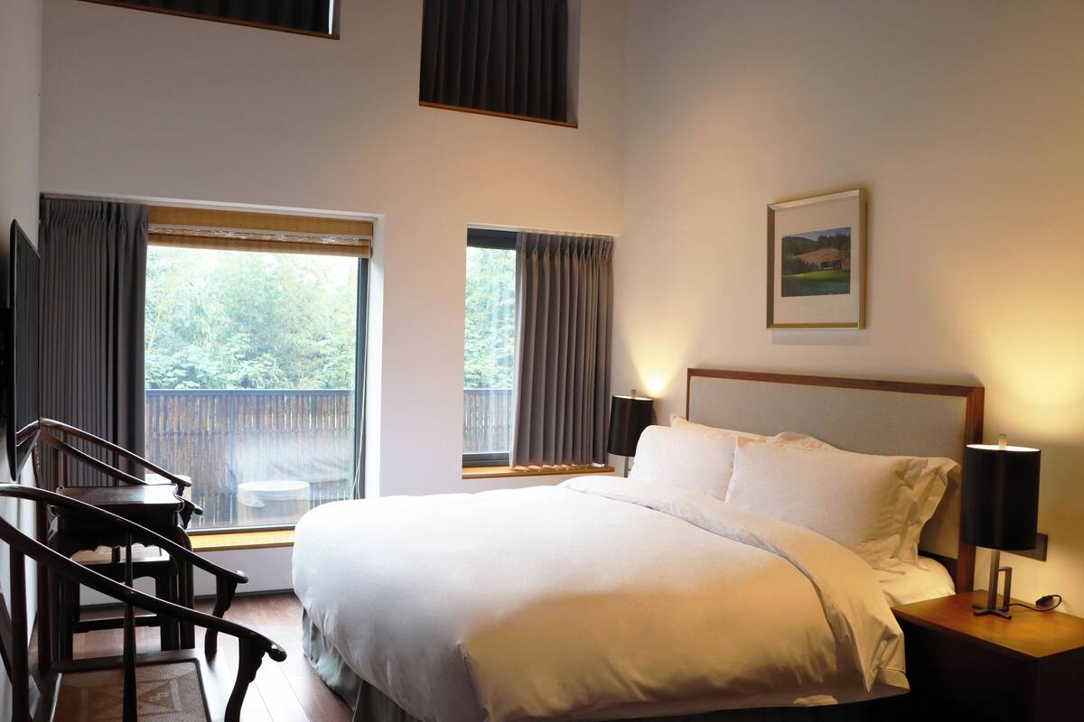 Una habitación de hotel con una cama grande, un escritorio y dos ventanas con cortinas.